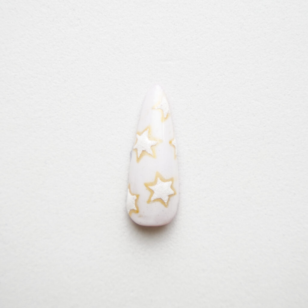 Tip de uña con un diseño de estrellas en tonos blancos y amarillos